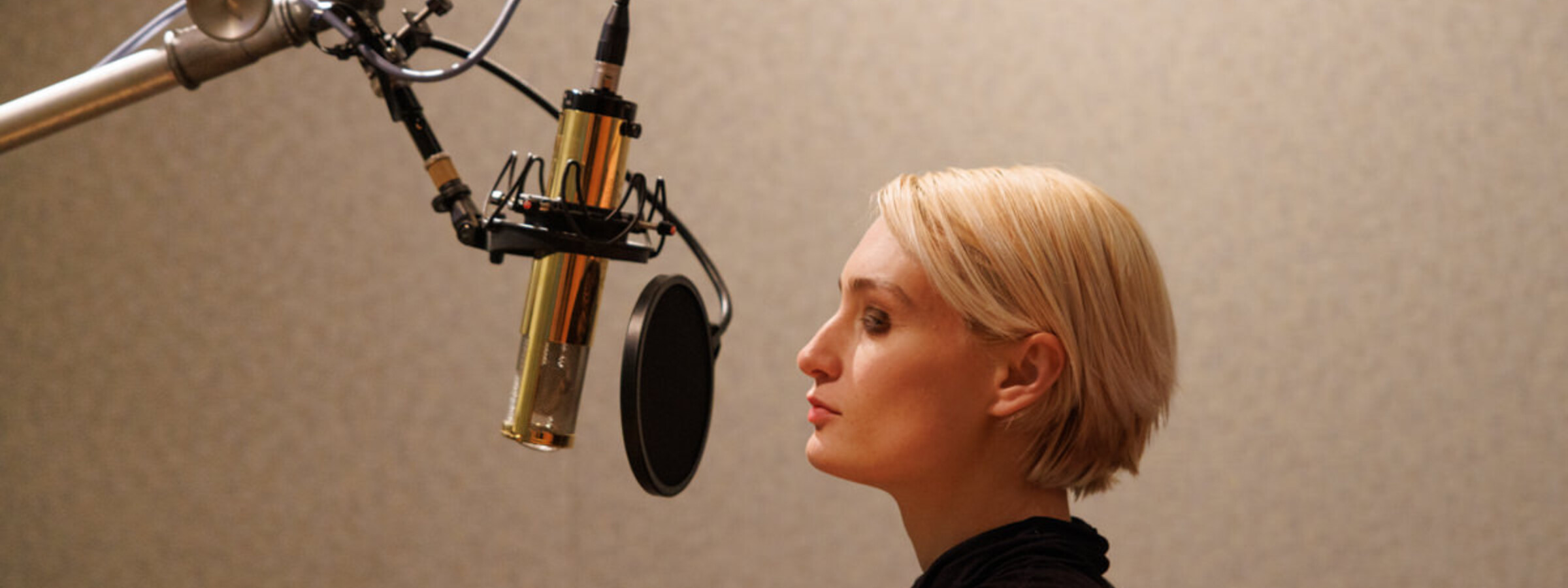 A singer with short blonde hair sings into a recording microphone