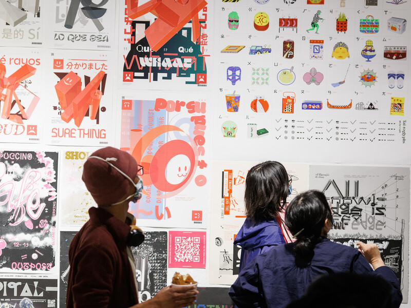 Three people standing in a gallery observing a wall filled with art posters