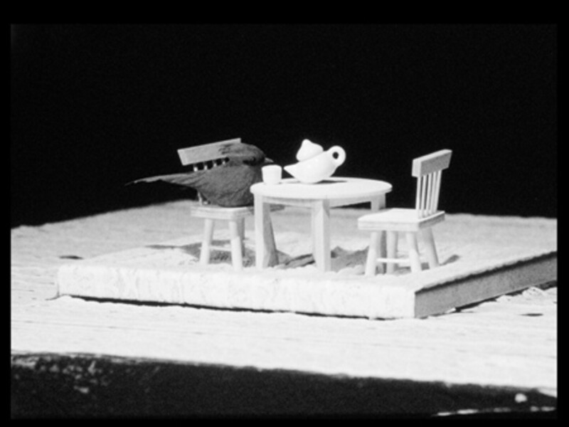 Black and white image with a bird figure having tea at a small table