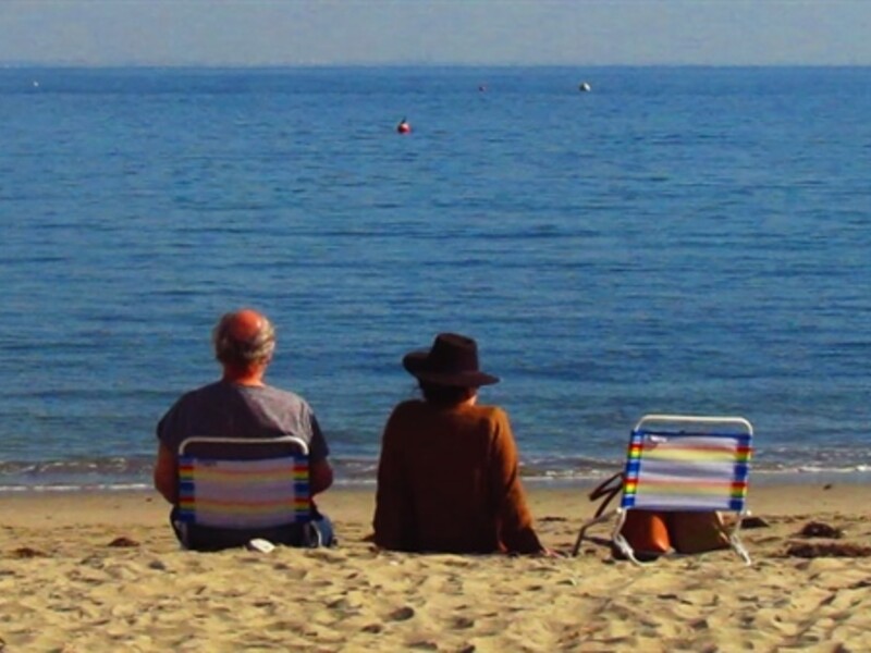 Image of two people sitting on a beach looking out at the water