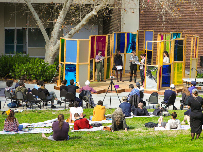 outdoor theater performance with audience members casually sitting on the lawn in front of the set outside of a school building