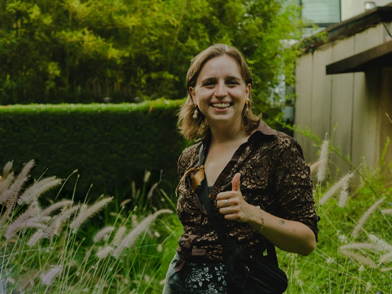 Allison (AC) Smith giving a thumbs up during a photo taken outdoors in an area with green plants