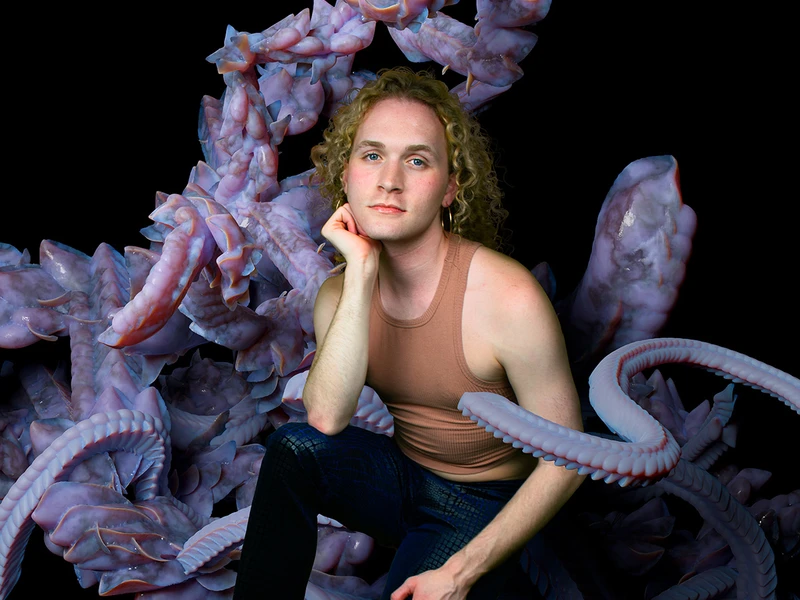 Caleb Craig posing with a large purple statue and a dark background