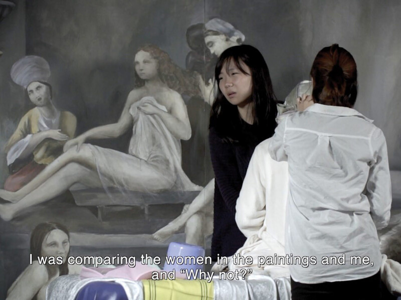 Two women, one with her back turned and one looking distraught, stand in front of a painting of figures. Text across the bottom of the image reads, “I was comparing the women in the paintings and me, and ‘Why not?”’