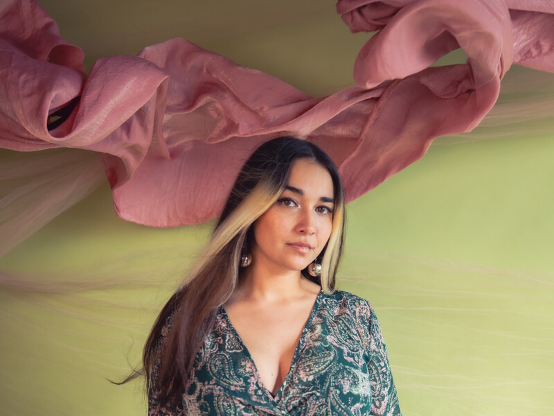 Profile photo of Zoe Moon, woman standing in flowered dress in front of a green wall