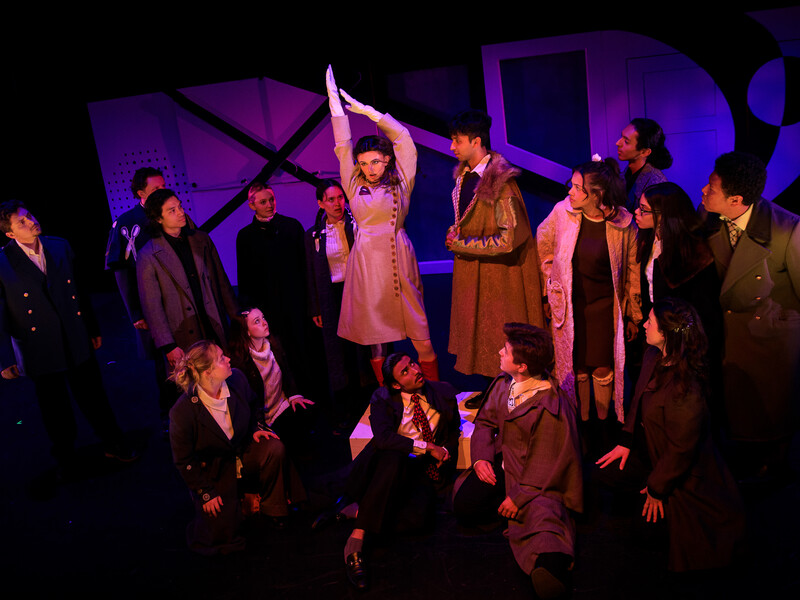 A group of people on a dimly lit theater stage focused on the person standing in the center