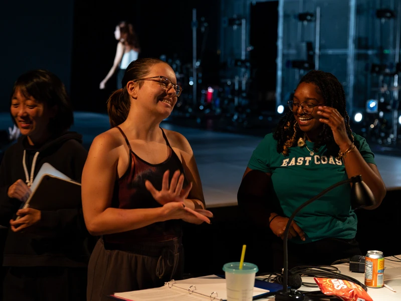 Women smiling together on set next to a work table
