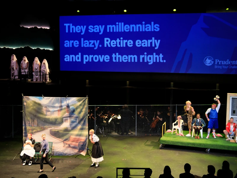 A large theater stage with numerous performers and a musical ensemble