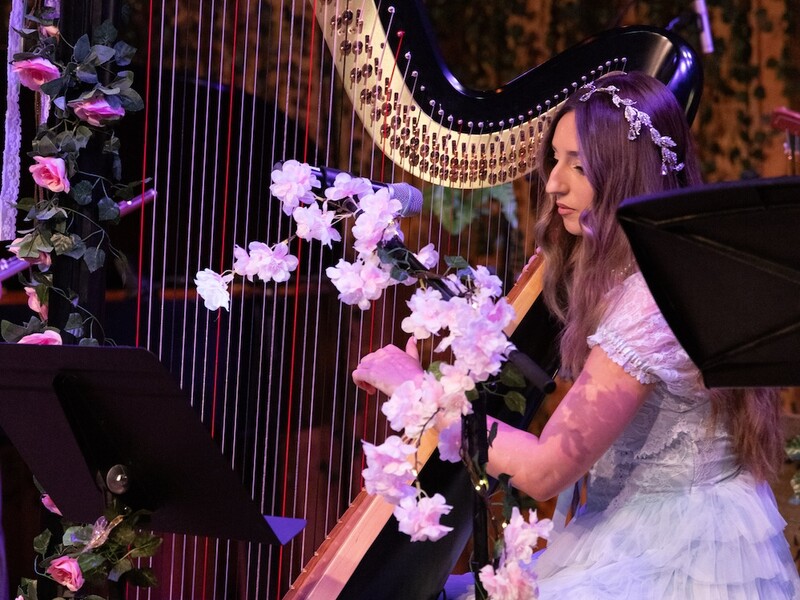 A woman in a white dress plays a harp decorated with flowers