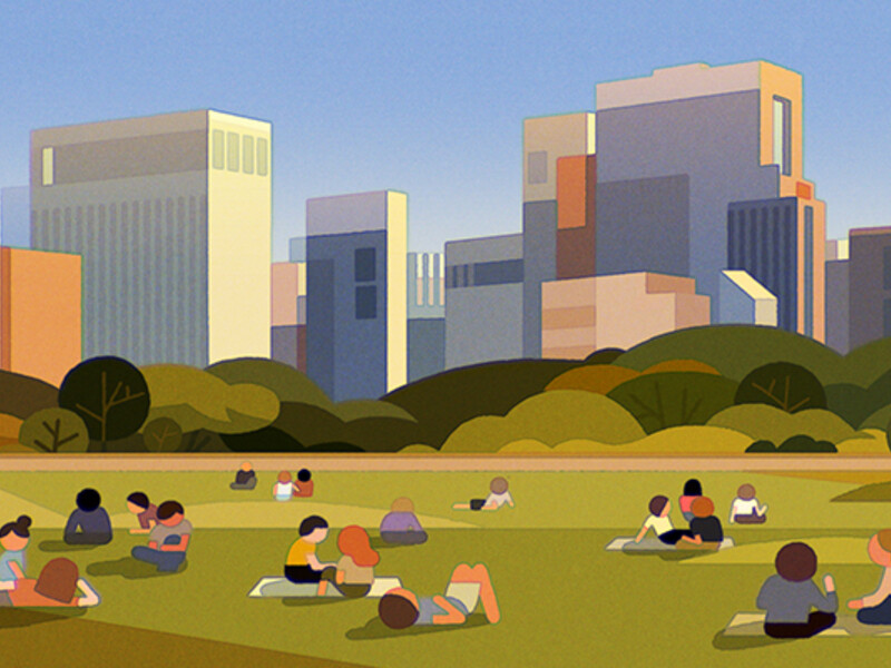 People sitting and lying on the grass in a park, with an urban skyline of modern buildings and trees in the background.