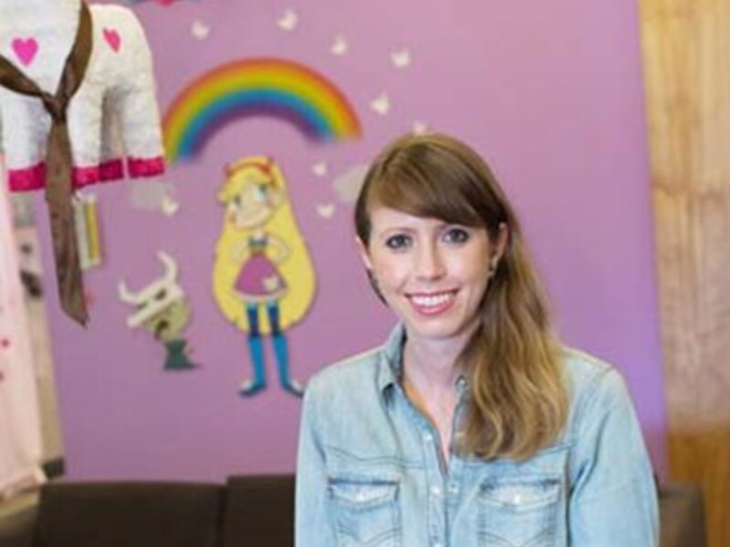 Woman in a denim shirt stands in front of a purple wall with a rainbow mural and character art.