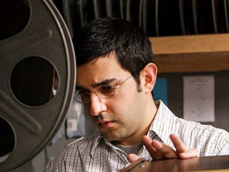 Man examines equipment in a film projection room beside a large film reel.