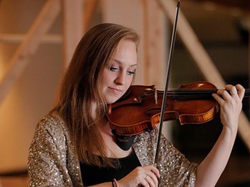 Person playing the violin indoors, wearing a sparkly shawl.