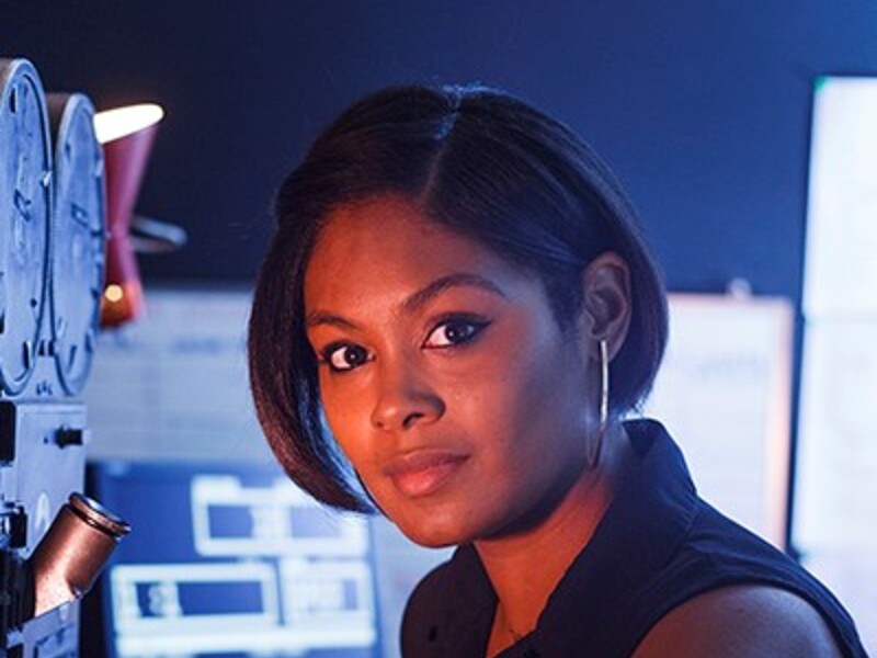 Woman in a dimly lit technical room with equipment and screens.