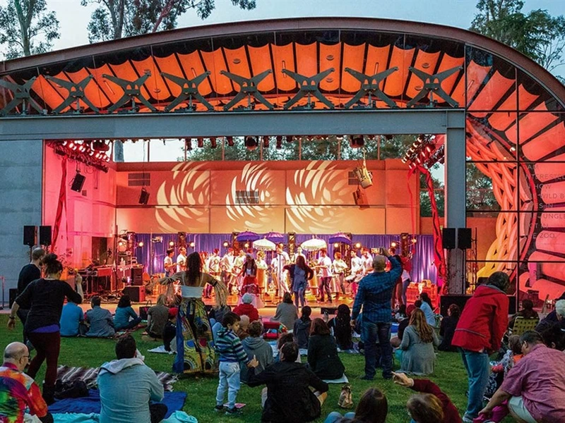 Outdoor performance at an amphitheater with a colorful stage and seated audience.