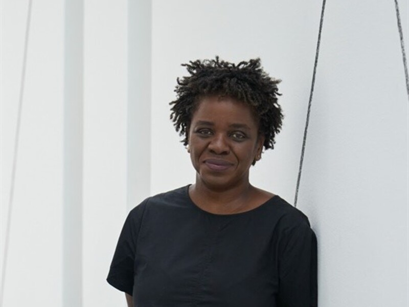 Person standing against a white wall with geometric line designs, wearing a black dress.