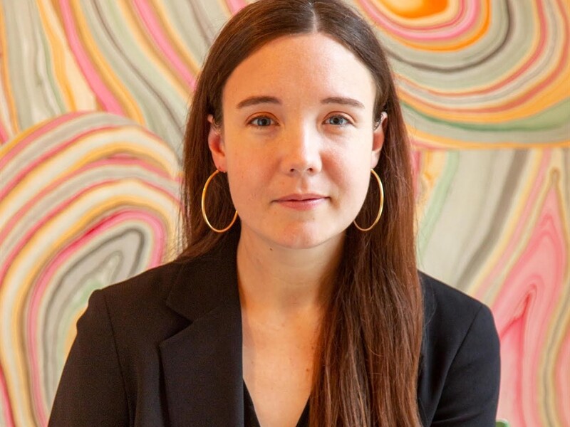 Person with long brown hair and hoop earrings against a colorful abstract background with swirling patterns.