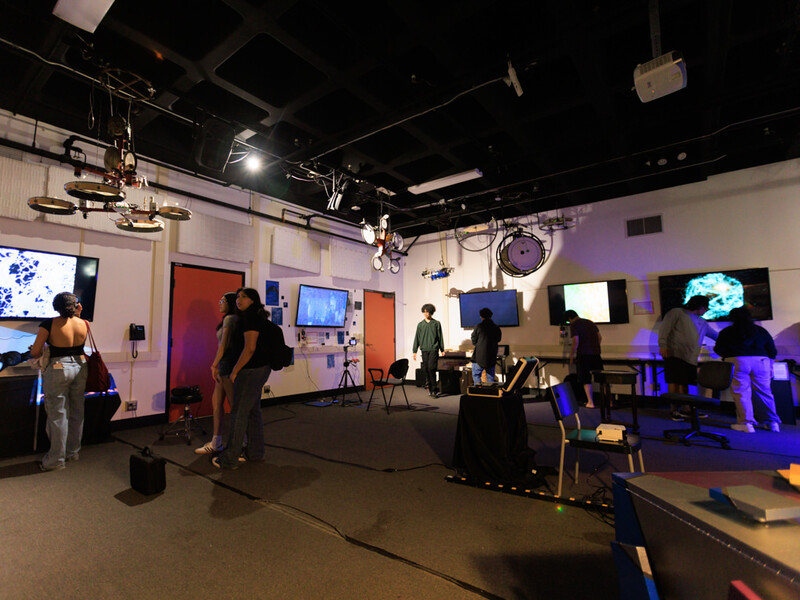 Indoor laboratory with people interacting with various monitors and technical equipment.