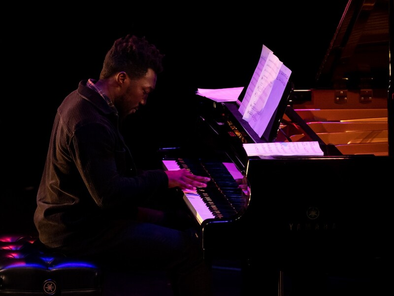 A close-up side view of a man playing a grand piano on a stage 