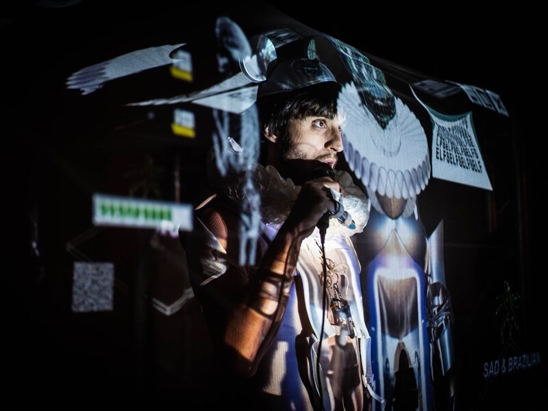 Man holding a microphone with colorful projections on him.