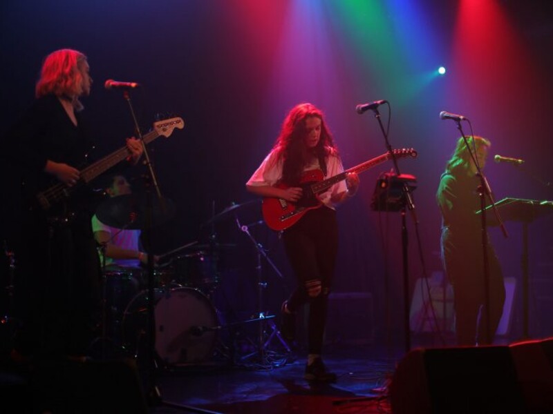 A band performing on a stage with colorful red, blue, and green lighting effects.