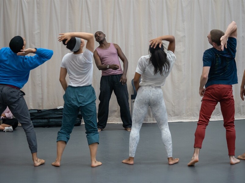 A group of dancers practicing movements in front of a light curtain, with an instructor leading