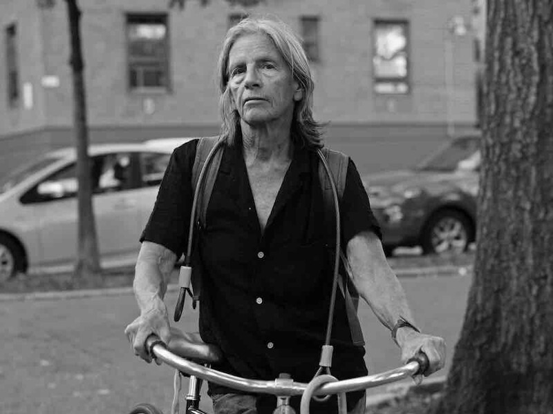 Eileen Myles, standing holding a bike, shot in black and white. 