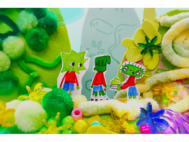 Three cartoon characters in a vibrant, green landscape with pom-poms and beads.