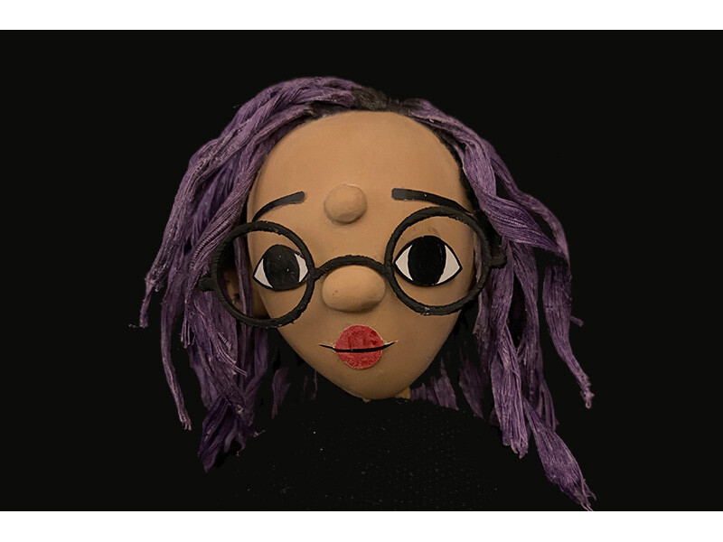 Clay head model with purple hair, black glasses, and red lips.