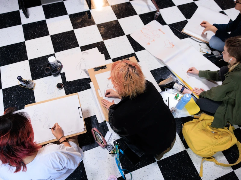 CalArts students sketch while seated on a black and white checkerboard floor. 