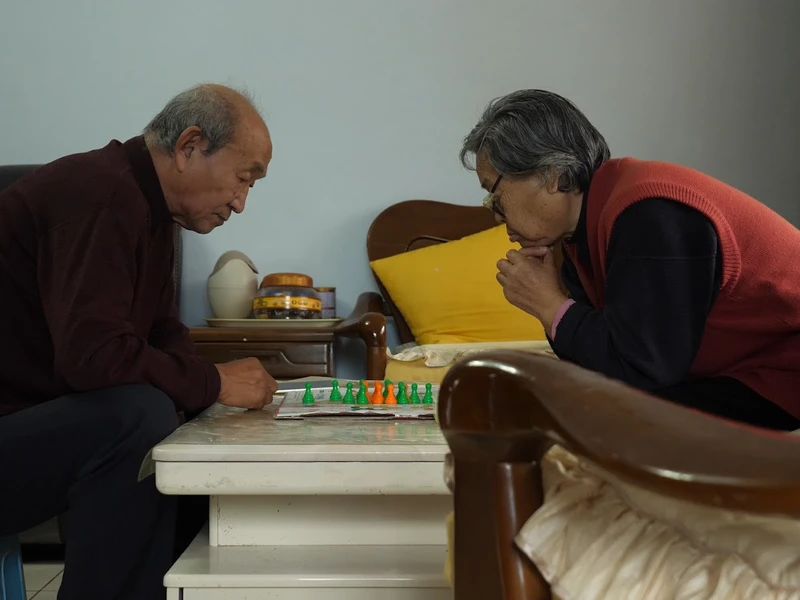 Two elderly individuals playing a board game at a small coffee table.