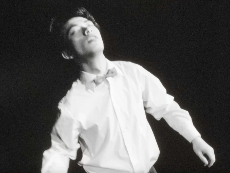 Black and white image of a person in a white shirt and bow tie with eyes closed.