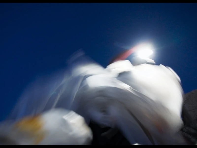 Blurry image with blue sky and bright light above white and gray shapes.