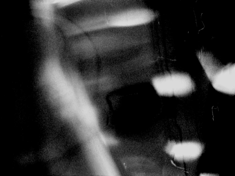 Abstract black and white image with blurred, grainy texture and light streaks.