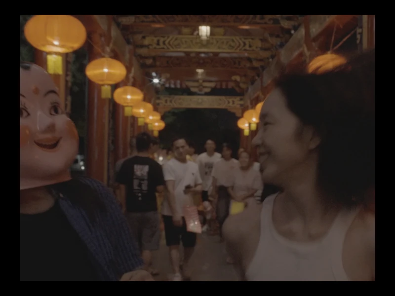 Two people walking under orange lanterns, one wearing a mask, the other smiling.