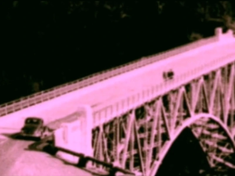 A sepia-toned image of a large arched bridge with a vintage car crossing.