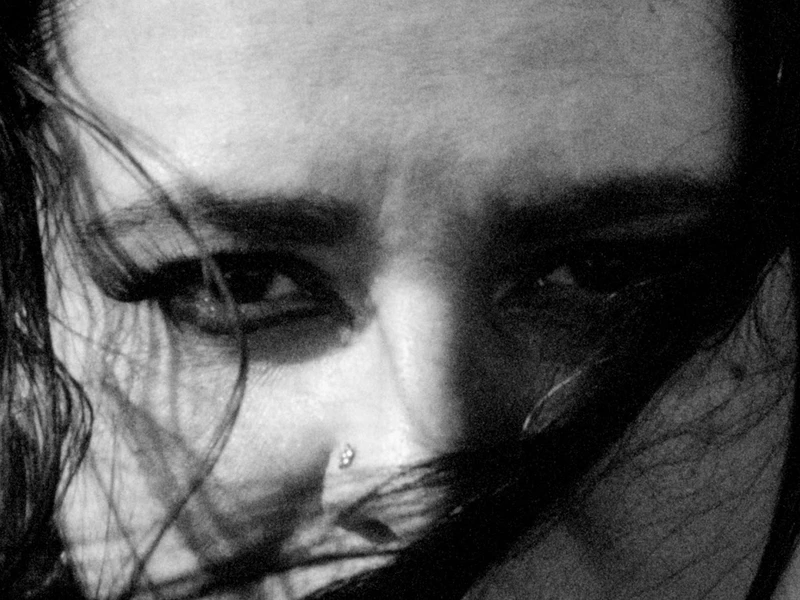 Close-up black-and-white image of eyes with hair partially covering the face.
