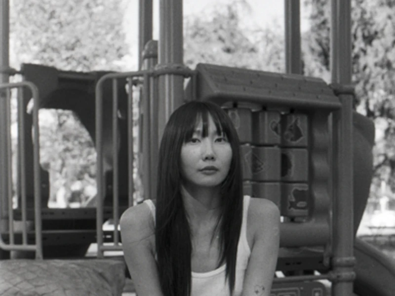 Black and white photo of Chorong Yang, staring directly into the camera, seated at a play ground. 
