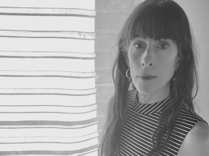 Image of a person in black and white, look at the camera, in front of a window. 