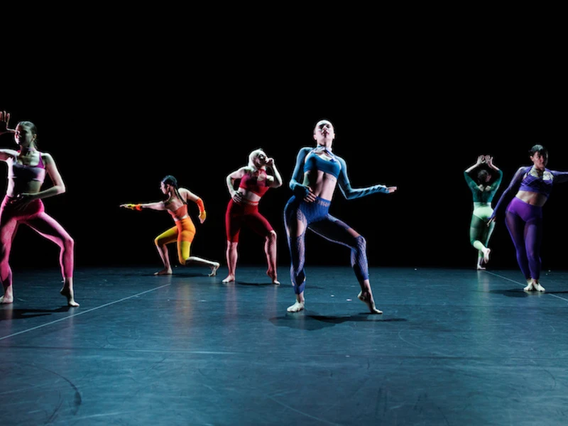 Six CalArts dancers perform on a darkened stage in a rainbow of leotard colors. 