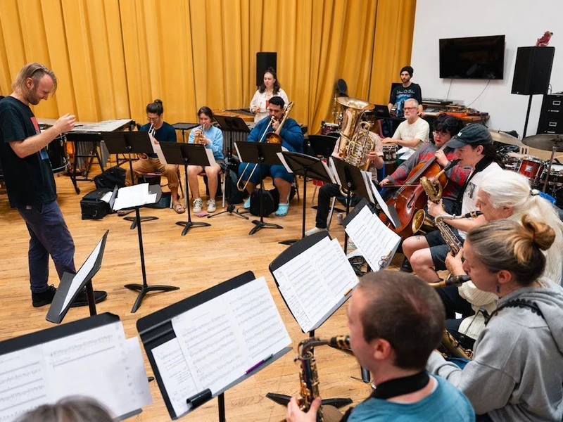 CalArts musicians perform in a semicircle, facing a conductor all in black. 