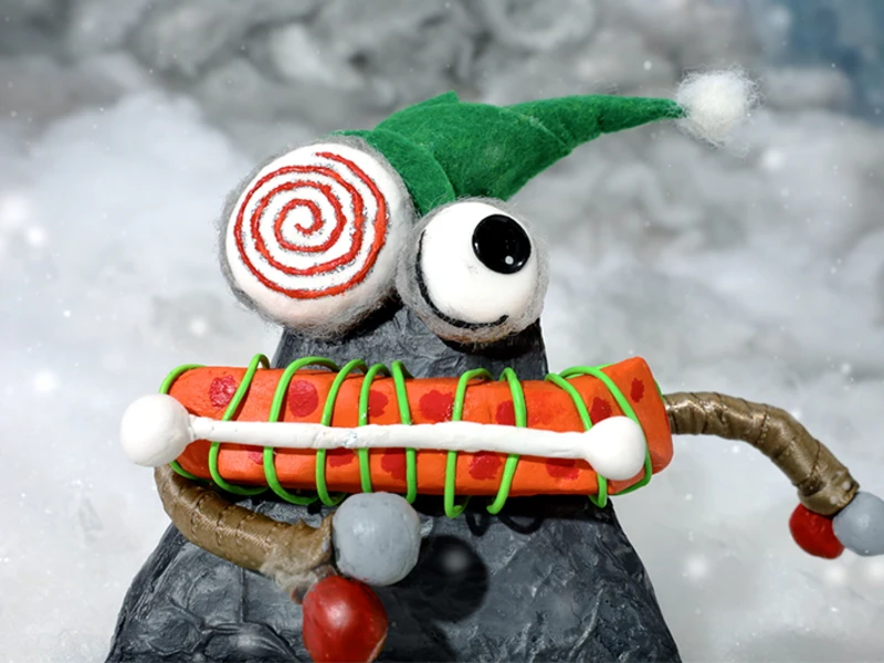 Clay figure with a green hat and a spiral eye in a snowy setting.