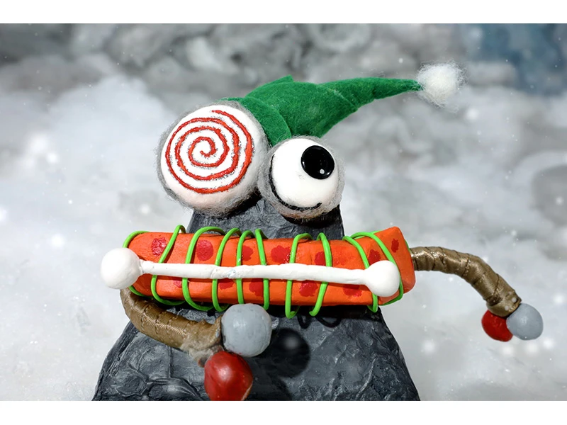 Clay figure with a green hat and a spiral eye in a snowy setting.