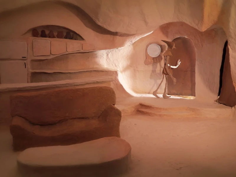 Cave-like interior with stone furniture and a humanoid figure walking through an archway.