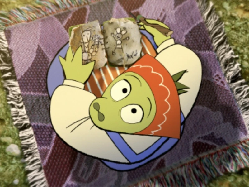 Animated green character with a red headscarf lying on a patterned blanket, holding drawings.
