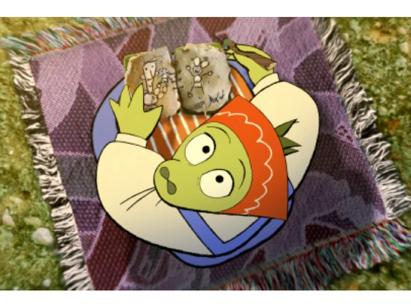Animated green character with a red headscarf lying on a patterned blanket, holding drawings.