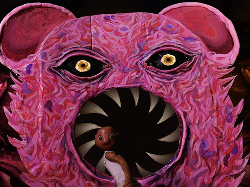 A colorful depiction of a pink bear face with sharp teeth and bright yellow eyes, featuring a small clay character in front.
