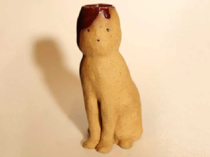 A small, beige ceramic figure of a seated animal with a dark red glaze on its head.