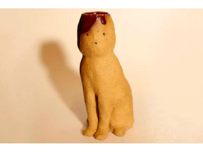 A small, beige ceramic figure of a seated animal with a dark red glaze on its head.