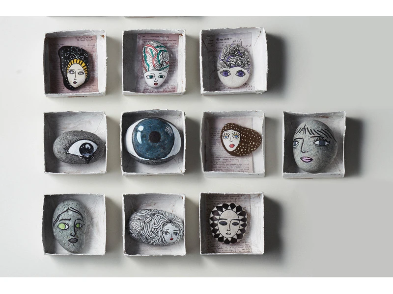 Twelve painted stones with stylized faces in square boxes.